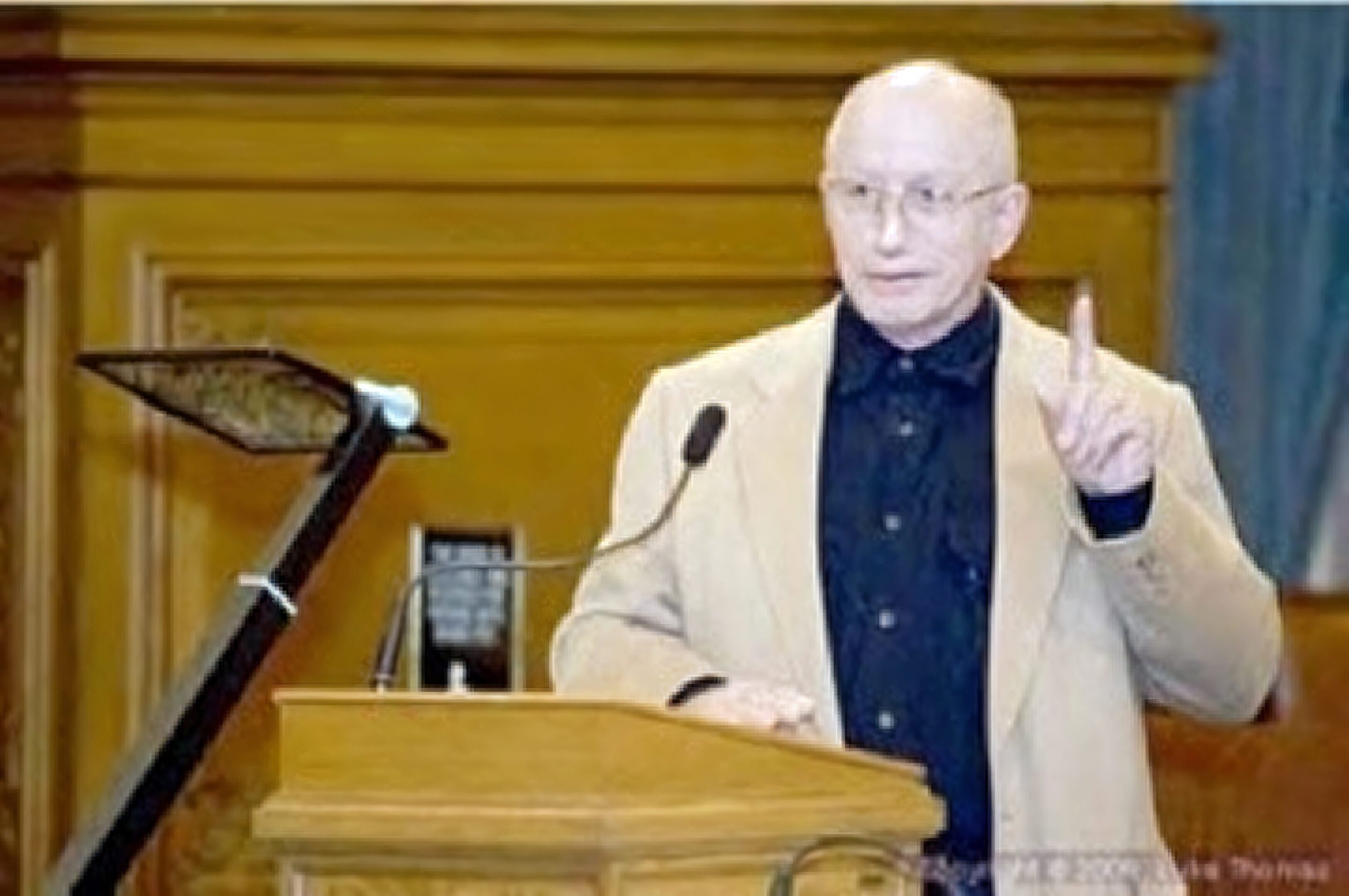Man speaking at podium with raised finger.