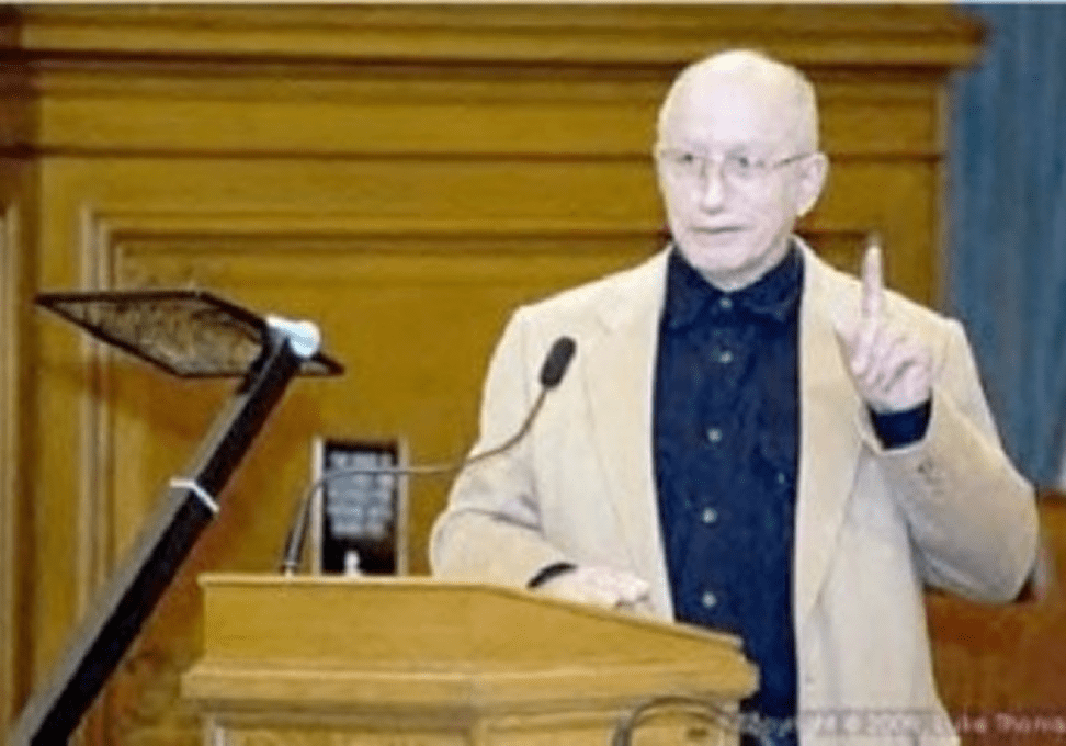 Man speaking at podium with raised finger.